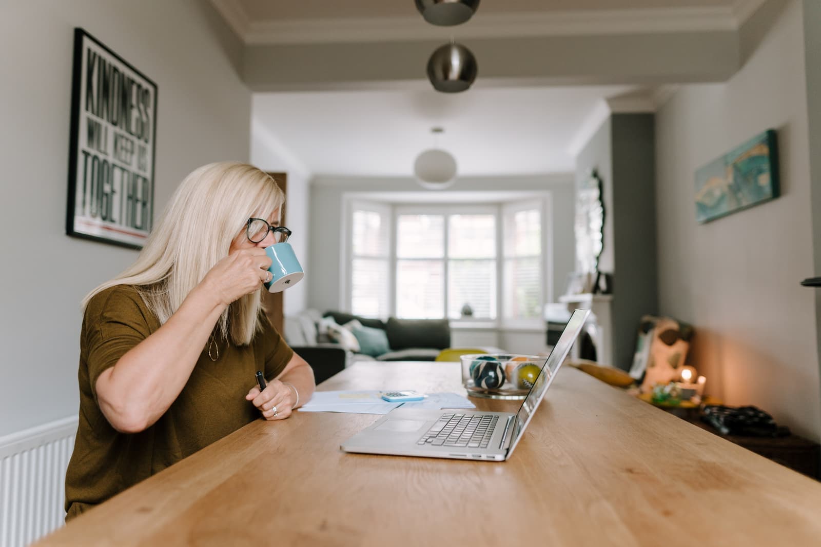 A woman at her kitchen table, calmly checking a letter against her laptop over a cup of tea